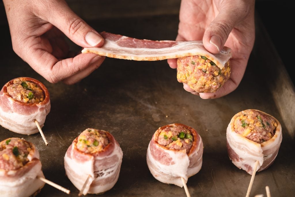 Meatballs getting wrapped in a slice of bacon.