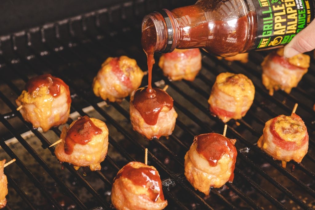 Meatballs on the smoker getting drizzled with BBQ sauce.