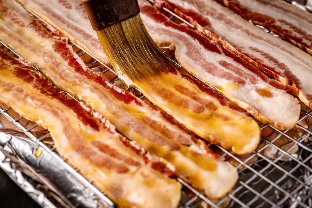 Bacon being brushed with maple syrup.