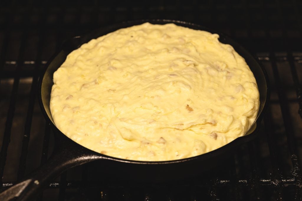 Mashed potatoes in a cast iron skillet on the grill grates of a smoker.