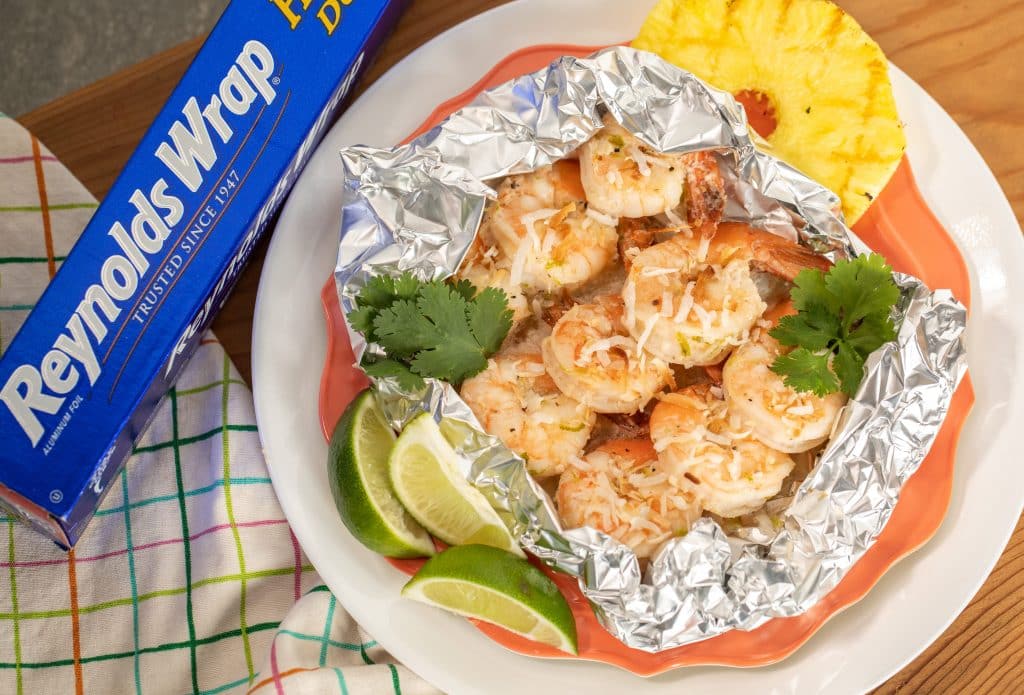 grilled coconut shrimp in foil packet with lime and grilled pineapple next to a package of Reynolds wrap aluminum foil.
