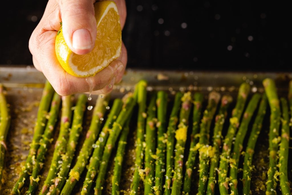 Lemon juice being squeezed over a row of asparagus.