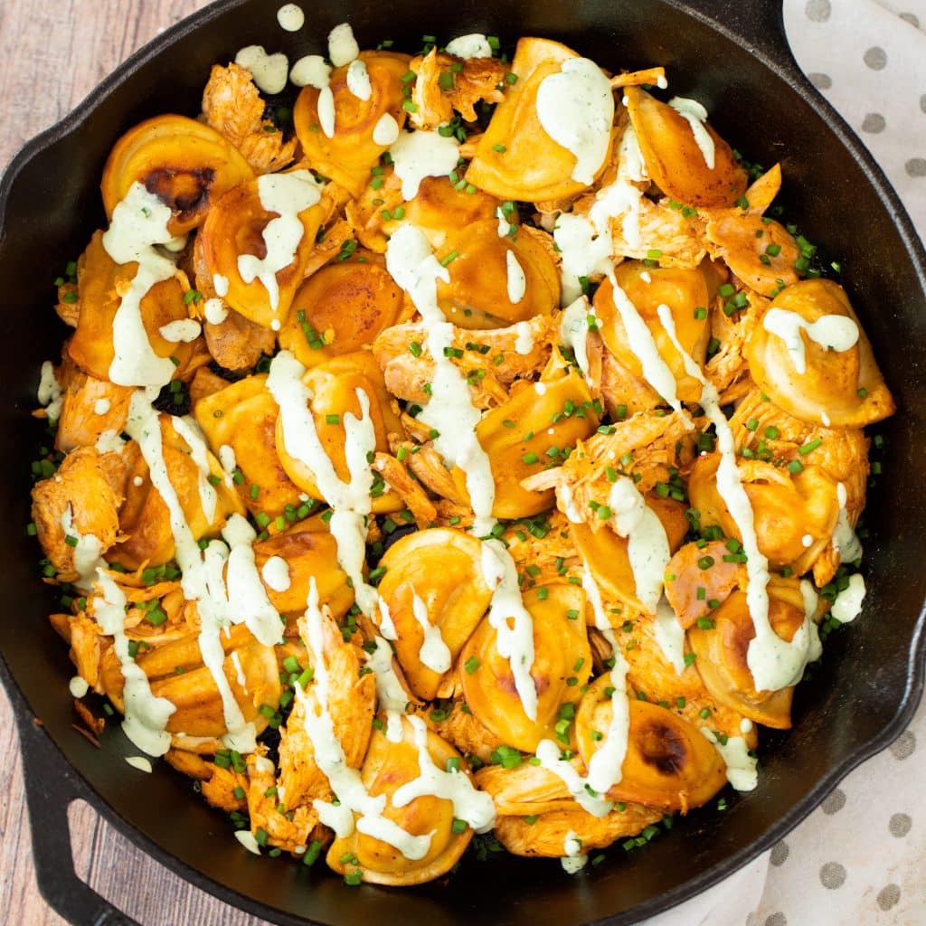 cast iron skillet filled with buffalo chicken and grilled pierogies and drizzled with homemade ranch dressing.
