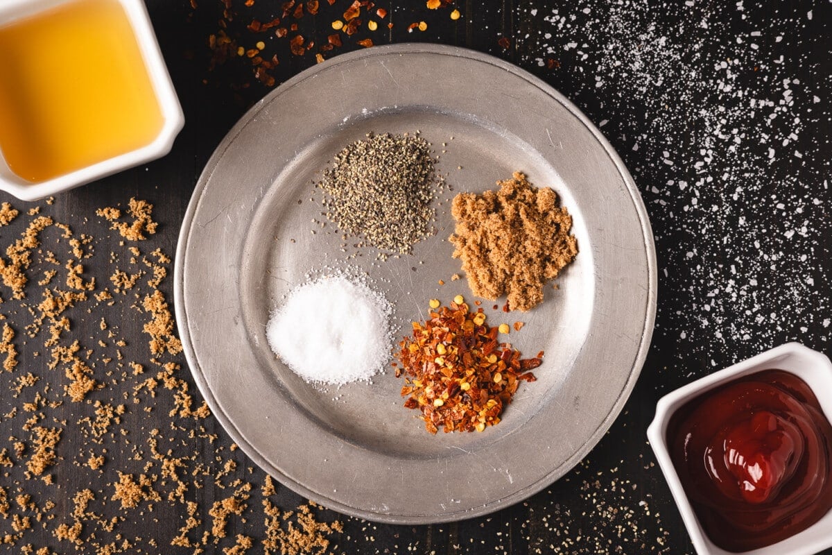 A plate with dry ingredients next to cups of vinegar and BBQ sauces.