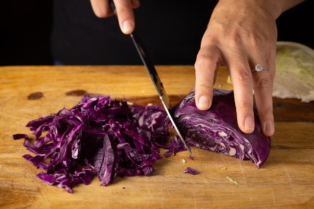 Red cabbage being chopped on a wooden board.