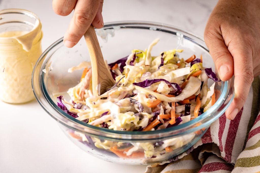 Coleslaw being stirred in a bowl.