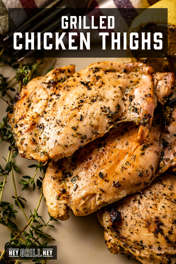 Three grilled chicken thighs in a pile next to fresh herbs with text overlay - Grilled Chicken Thighs.