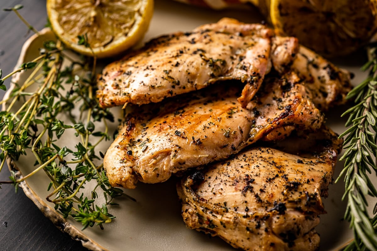 Three grilled chicken thighs in a pile next to fresh herbs.