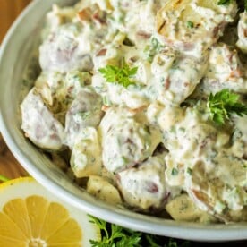 Grilled potato salad in a bowl with a lemon wedge next to it.