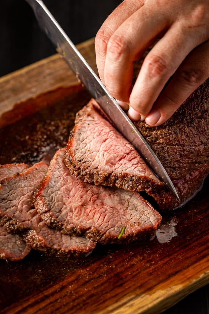 Grilled tri tip roast being sliced on a cutting board.