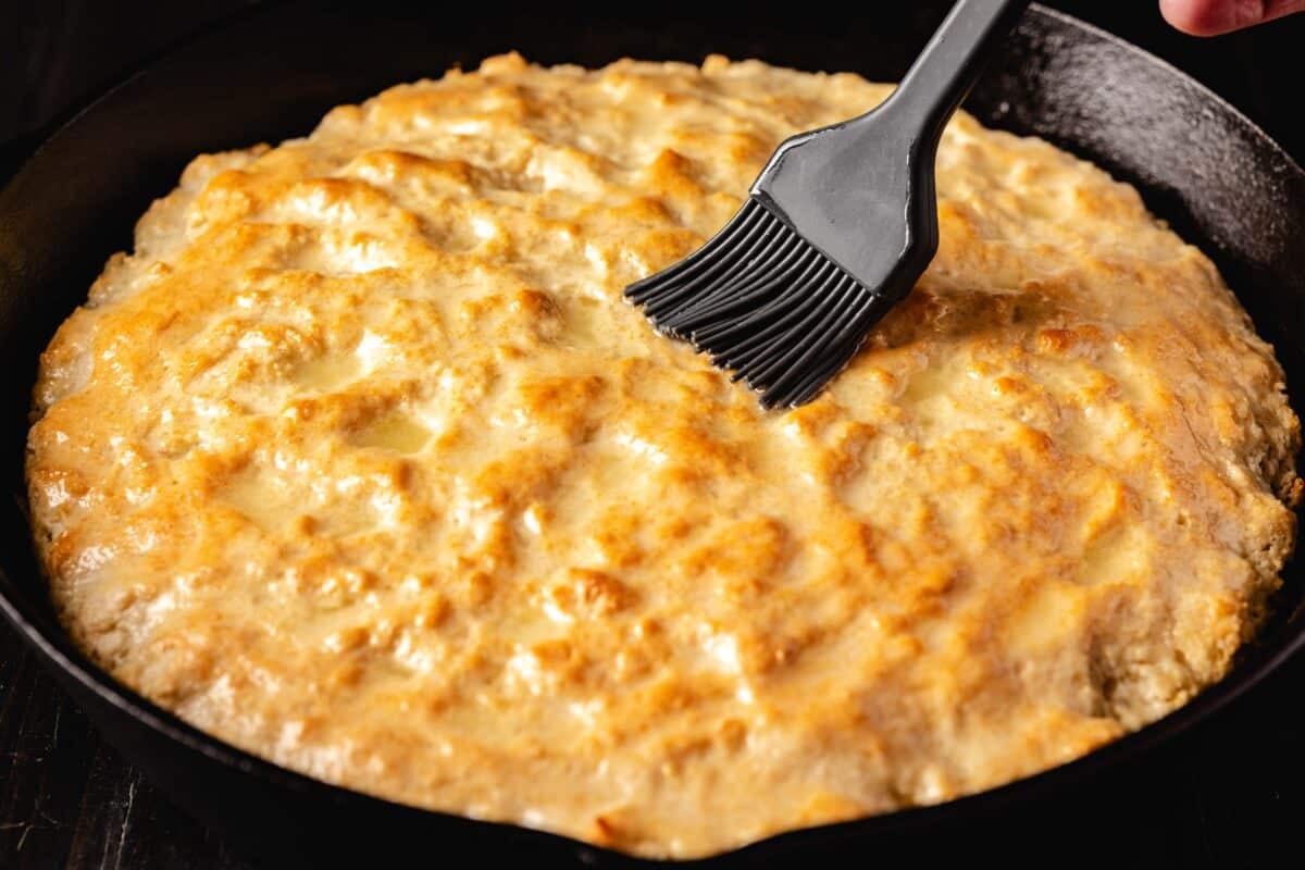 A rubber basting brush applying butter to the top of skillet biscuits.