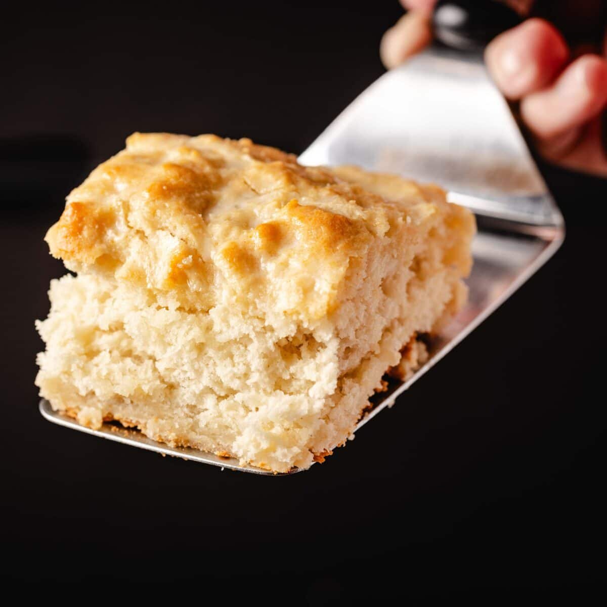 A metal spatula holding homemade biscuit over a black background.