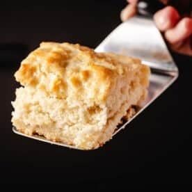 A metal spatula holding homemade biscuit over a black background.