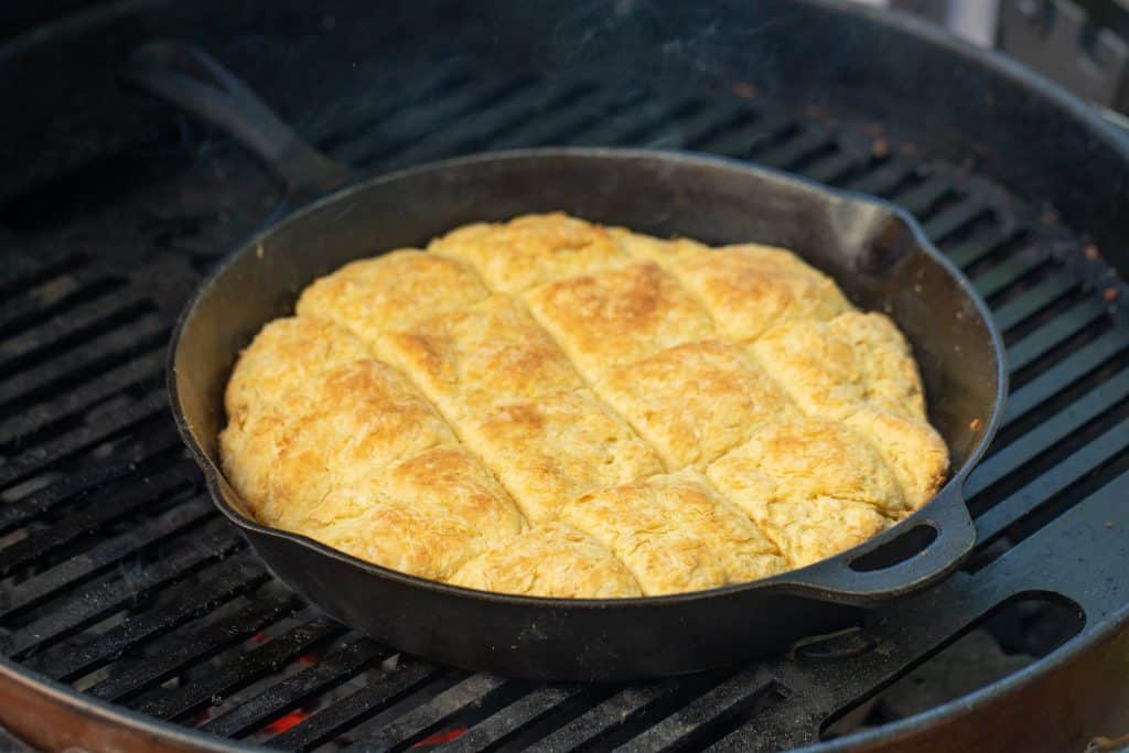 cast iron skillet with biscuits on a charcoal grill.