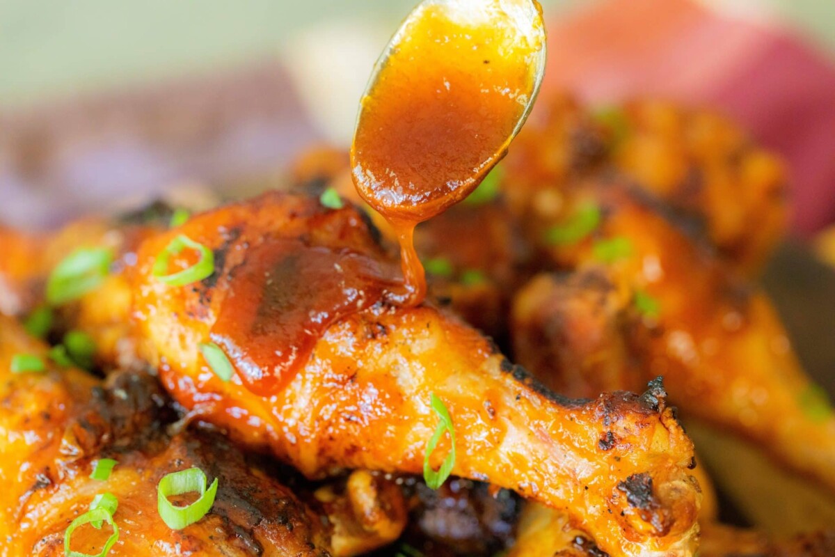 Chicken drumsticks being drizzled with sauce from a spoon.