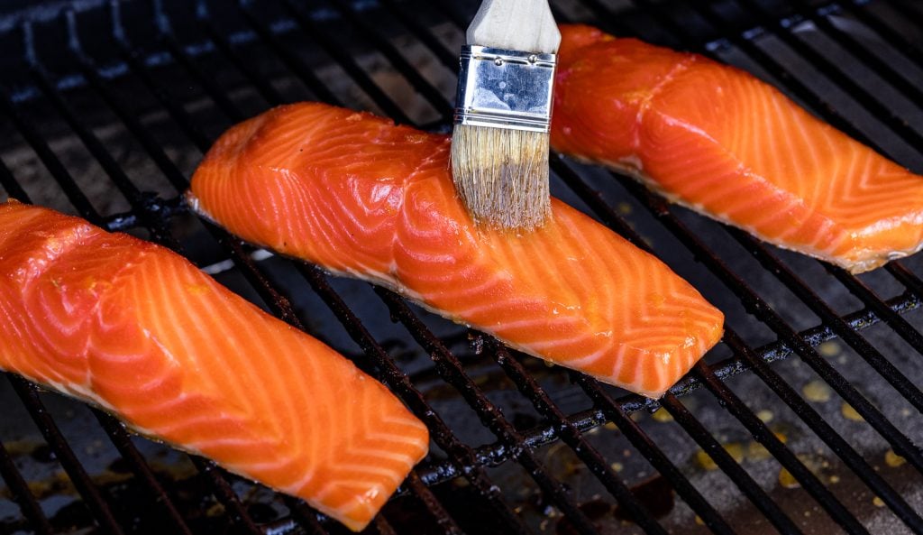 Orange maple glaze being brushed on a salmon filet on the smoker.