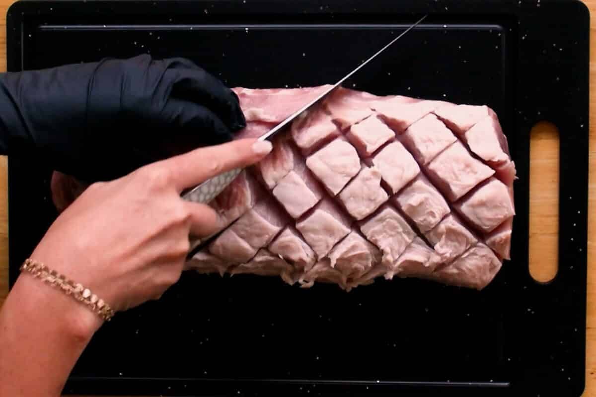 A chef's hand scoring the top of a loin cut with a knife.