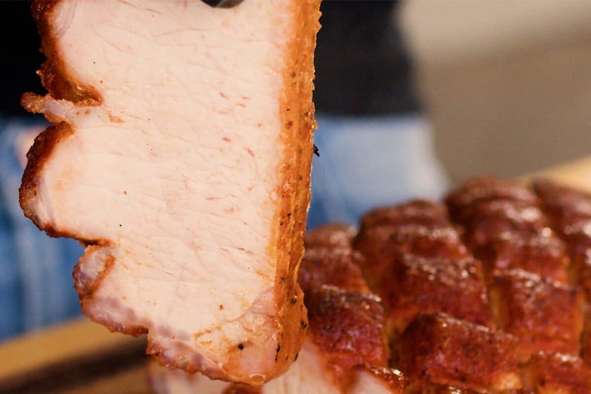 A slice of pork loin held up in front of a full roast.