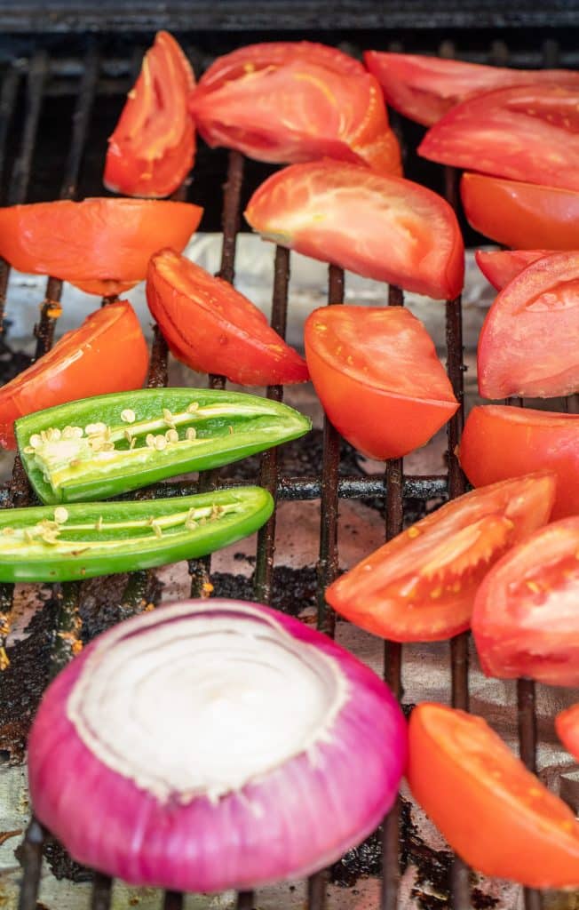 tomatoes, jalapenos, and a purple onion sliced and on the grill grates inside the grill.
