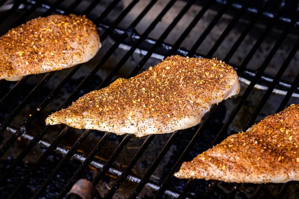 Seasoned chicken breasts on the grill grates of a smoker.