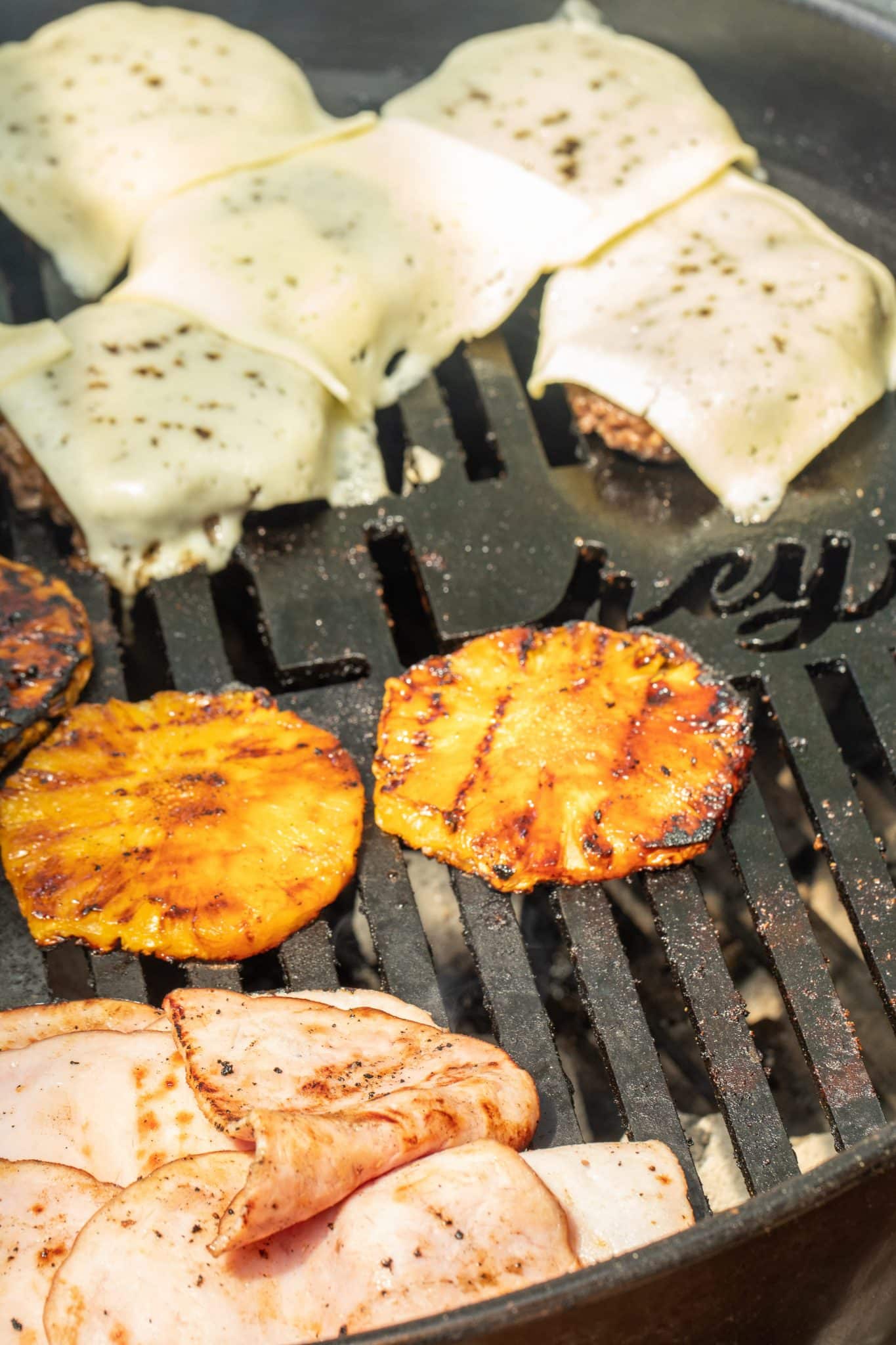 Cheese topped burger patties on the grill with grilled pineapple and ham