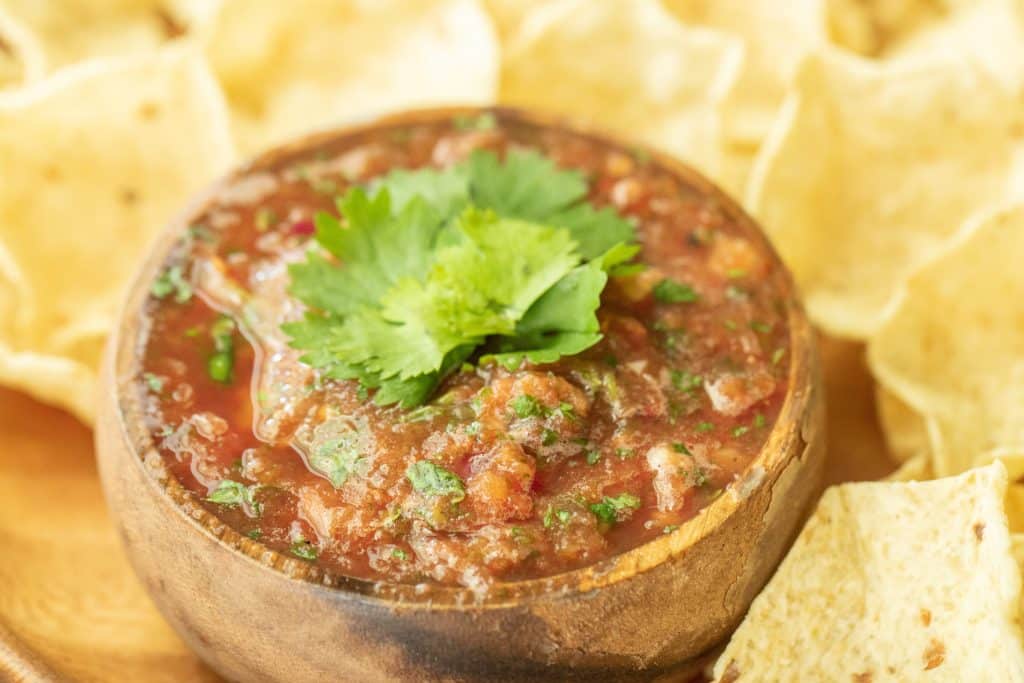 wooden bowl full of smoked salsa, surrounded by a plate of tortilla chips.