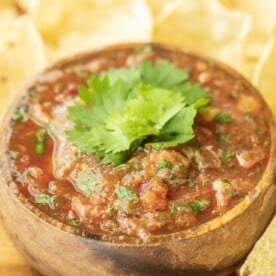 Smoked salsa garnished with fresh cilantro in a round wooden bowl surrounded by corn tortilla chips.