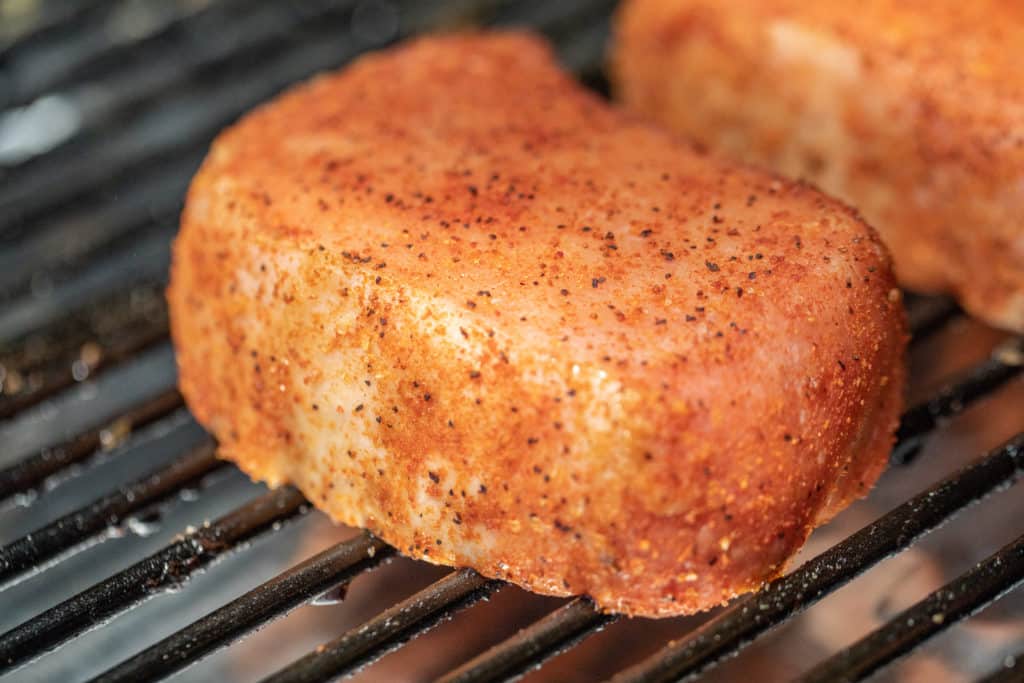 pork chop with seasoning on the grates of a smoker.