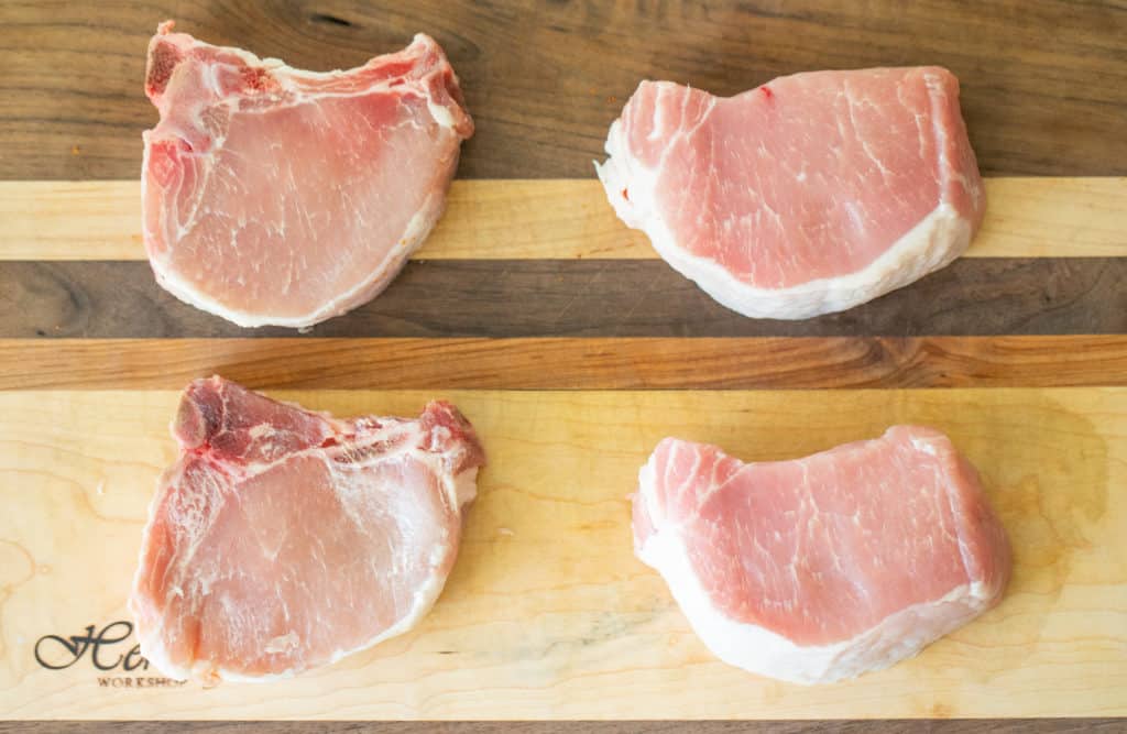 2 bone in pork chops and 2 boneless pork chops on a wooden cutting board.
