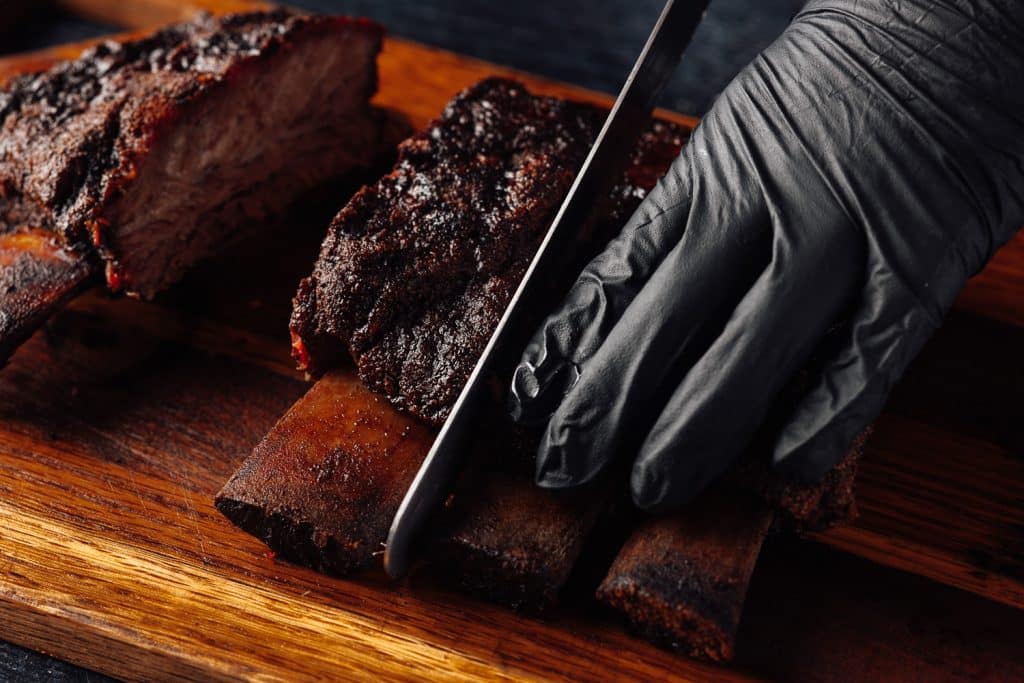 Beef ribs being sliced on a wooden cutting board.