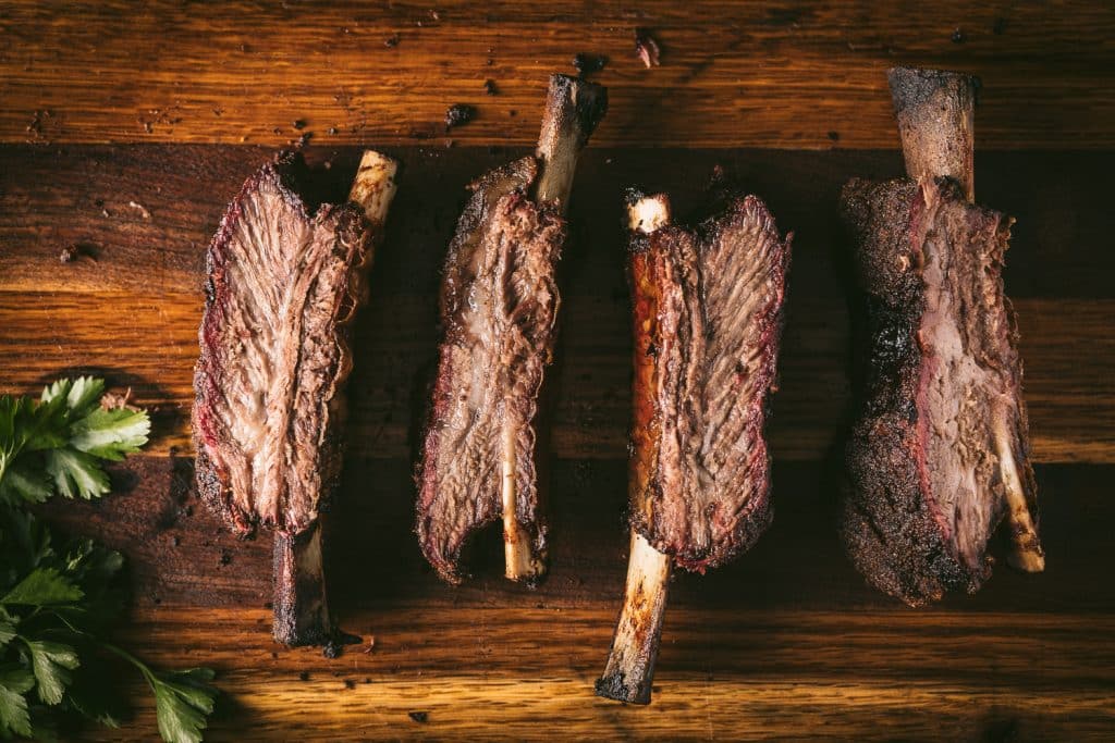 Four beef ribs lined up on a wooden cutting board.