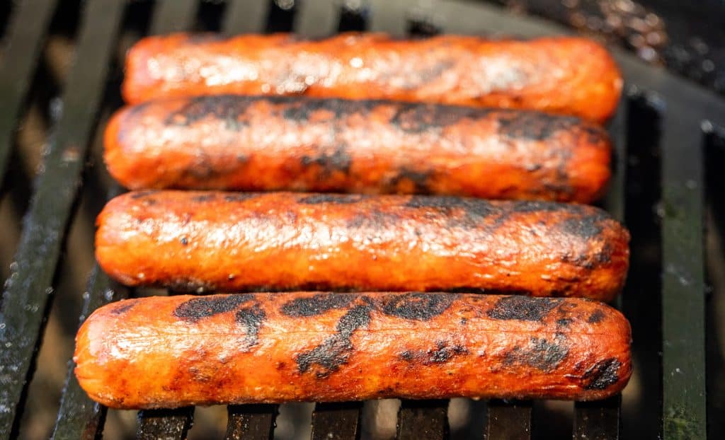 Hot dogs cooking on a charcoal grill.