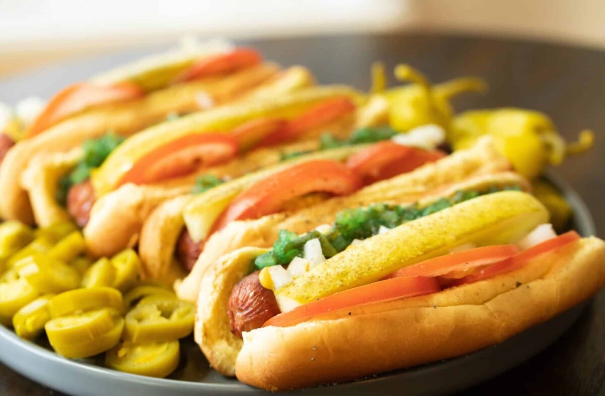 Cooked frankfurters on buns topped with sliced tomatoes, pickles, and relish.