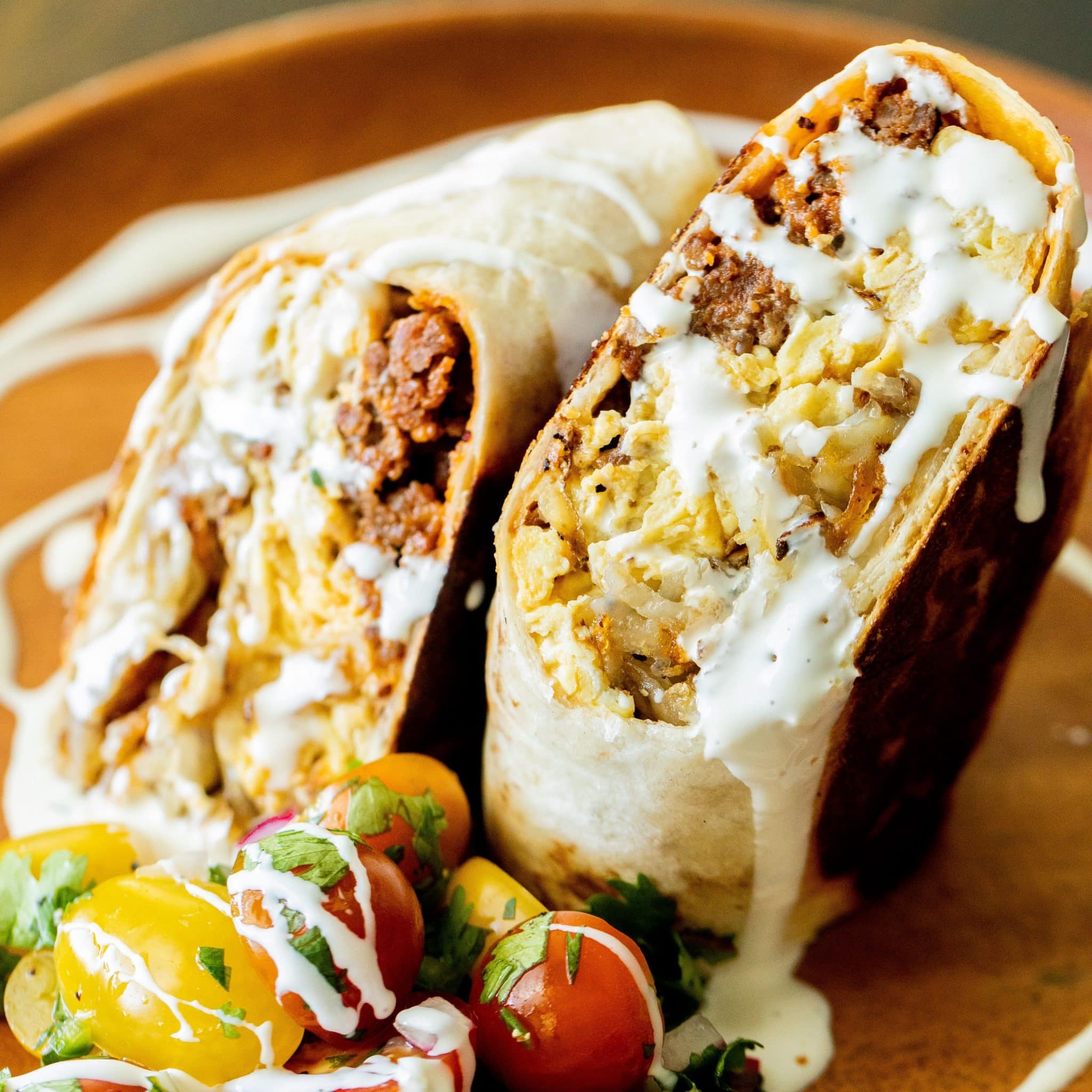 A burrito cut in half on a bias drizzled with sauce on a plate.