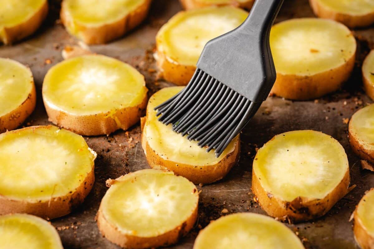 Potato slices on a baking sheet being brushed with oil.