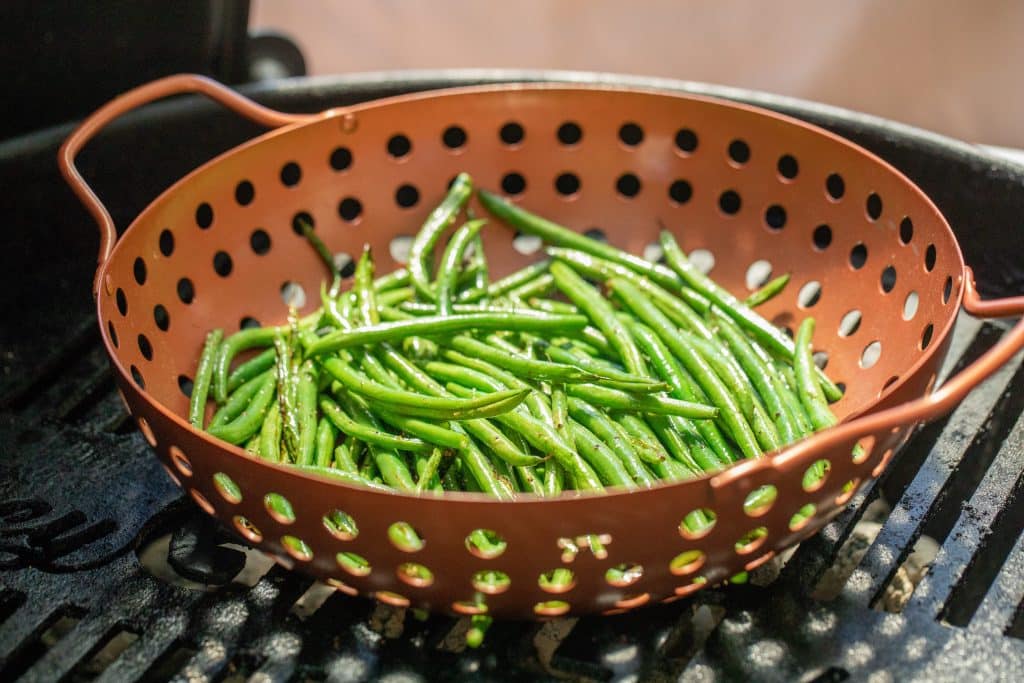 Fresh green beans in a vegetable grilling basket on a charcoal grill.