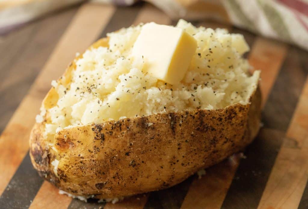 cube of butter on an open baked potato on a wooden cutting board