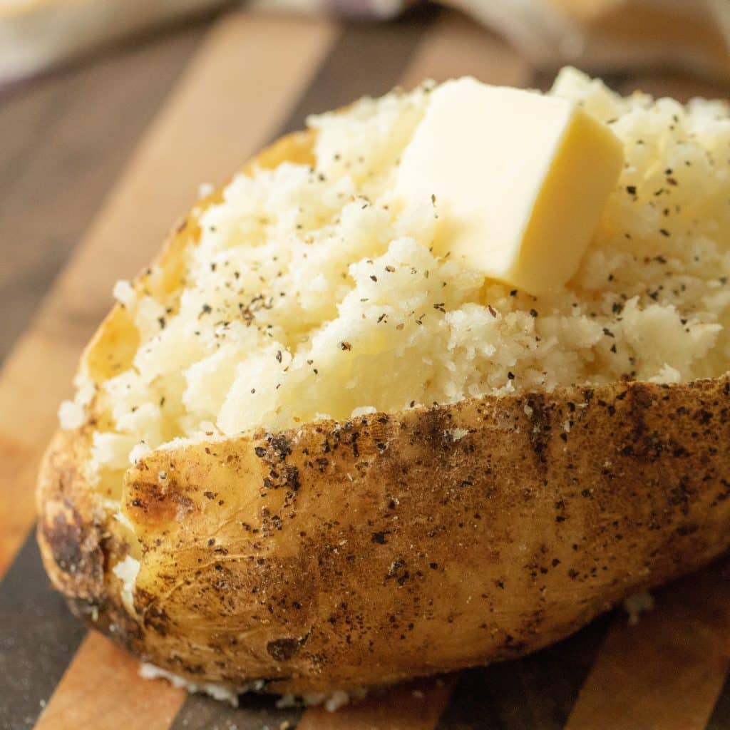 Grilled baked potato topped with pepper and a slice of butter.