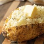 Sliced and fluffed grilled baked potato topped with salt, pepper, and a pad of butter.