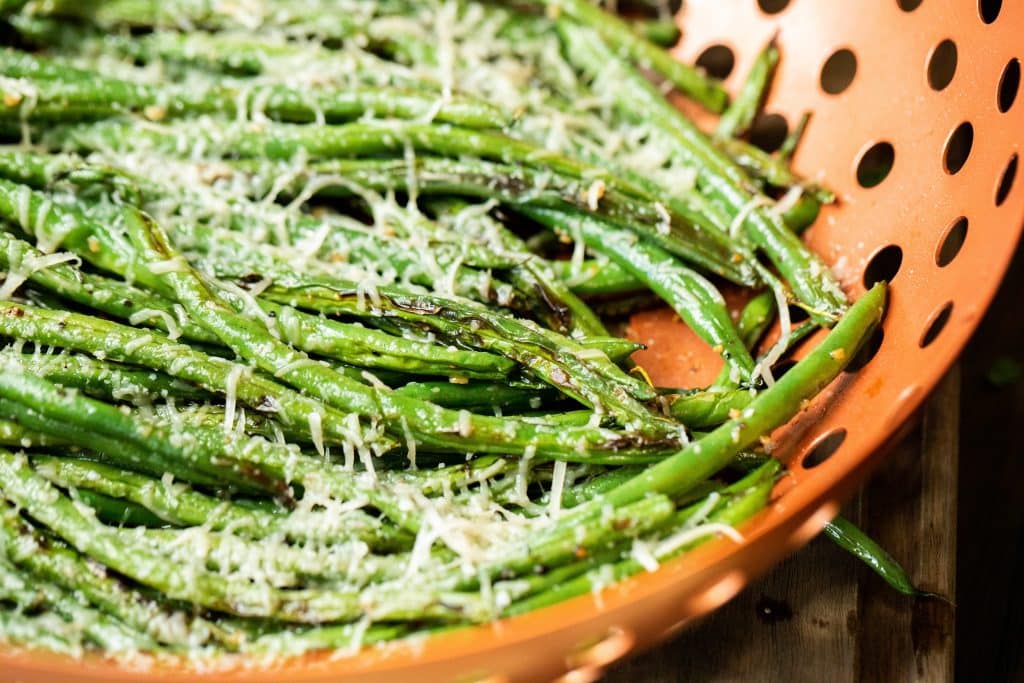 Close up of garlic parmesan grilled green beans in a grilling basket.