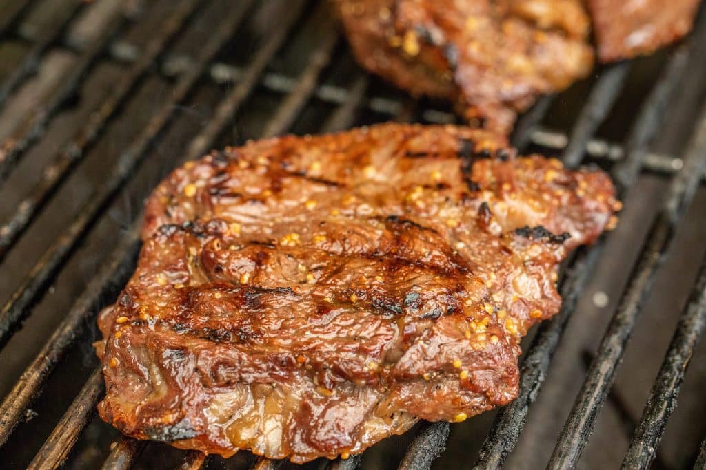 Marinated steak cooking on a grill.