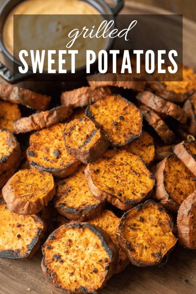 grilled sweet potatoes on a wood cutting board with dipping sauce on the side in a cast iron bowl.