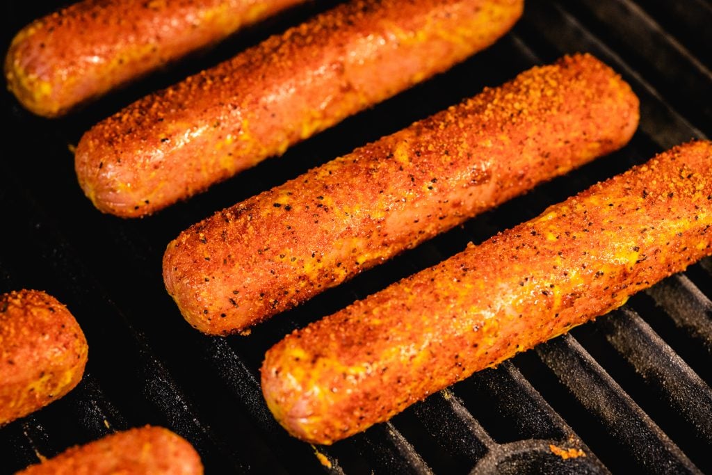 Seasoned hot dogs on the grill grates of a smoker.