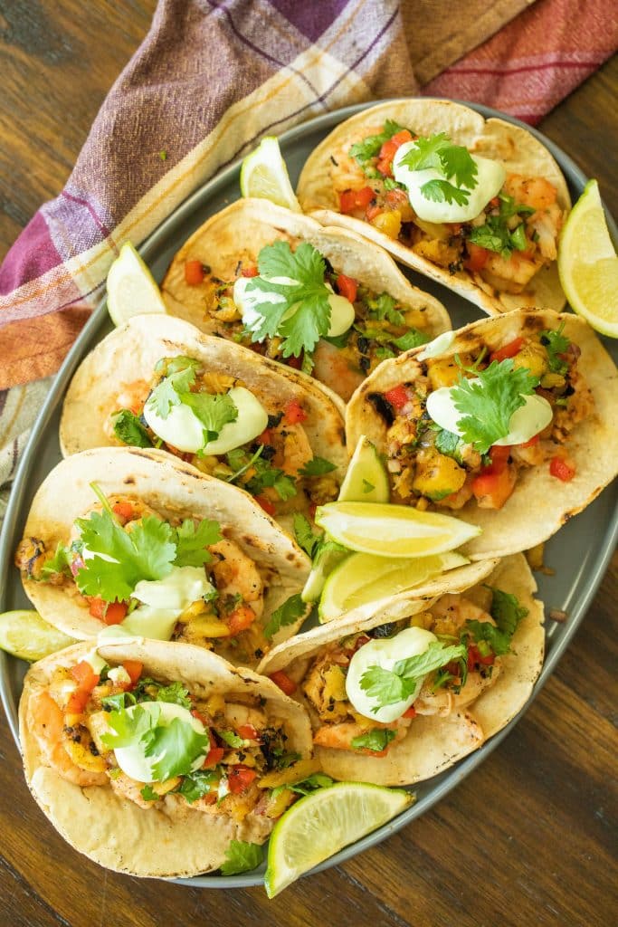 Grilled shrimp tacos on a platter with lime wedges.