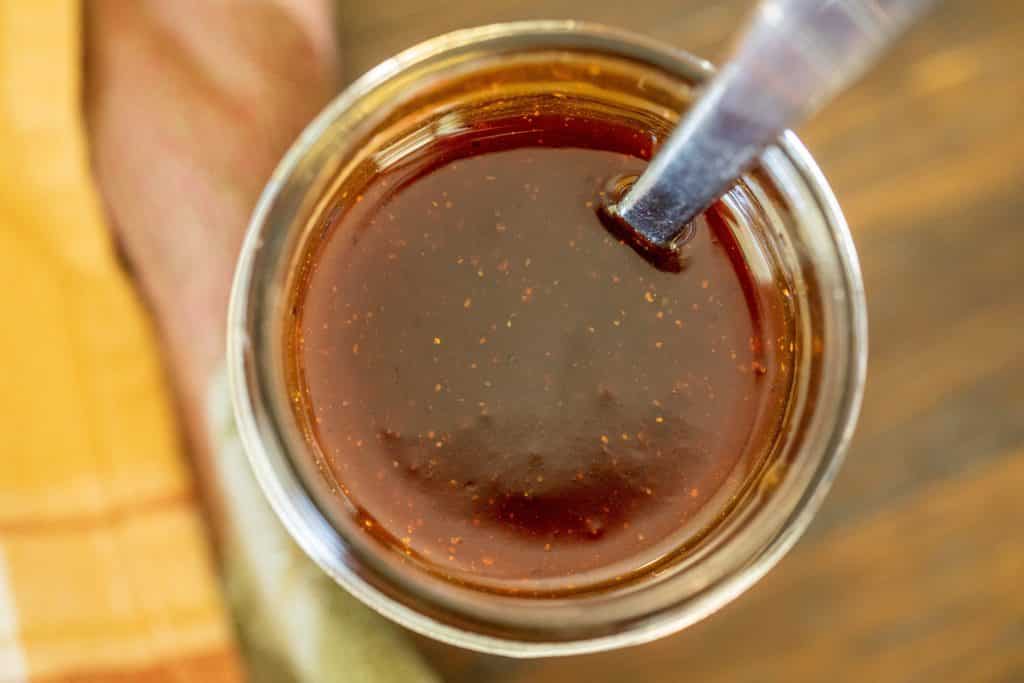Overhead view of maple bourbon glaze in a glass jar with silver spoon.