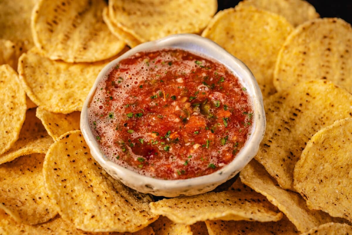 A white bowl filled with salsa surrounded by yellow tortilla chips.