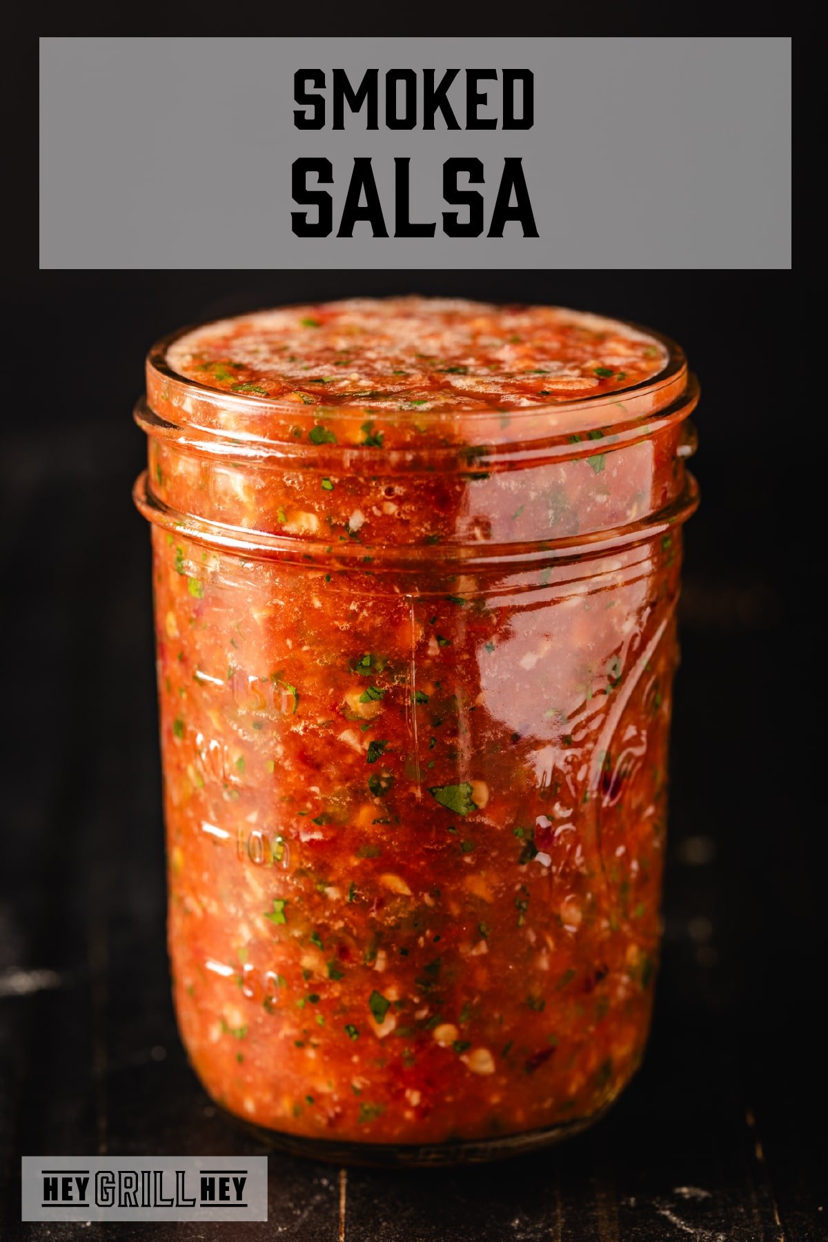 smoked salsa A mason jar filled with salsa sitting on a dark surface. The text overlay reads "Smoked Salsa" at the top, and "Hey Grill Hey" at the bottom.