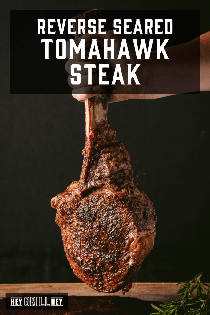 Grilled tomahawk steak being held by the bone with text overlay - Reverse Seared Tomahawk Steak.