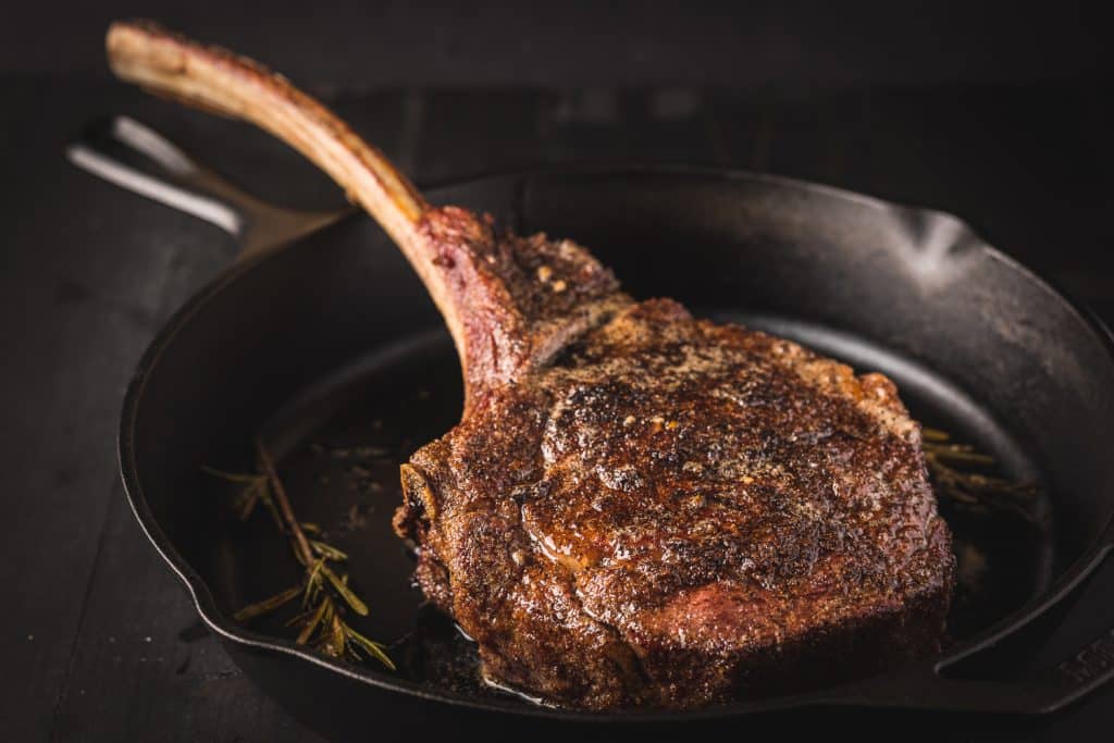 Tomahawk steak being seared in a cast iron skillet.
