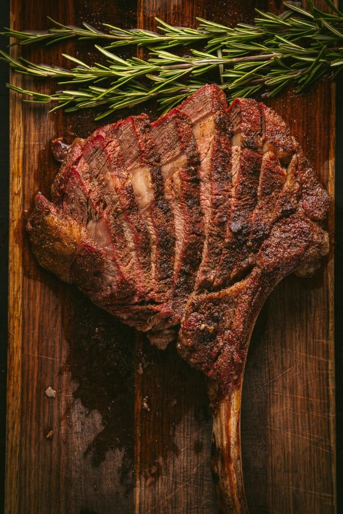 Sliced tomahawk steak on a wooden cutting board.